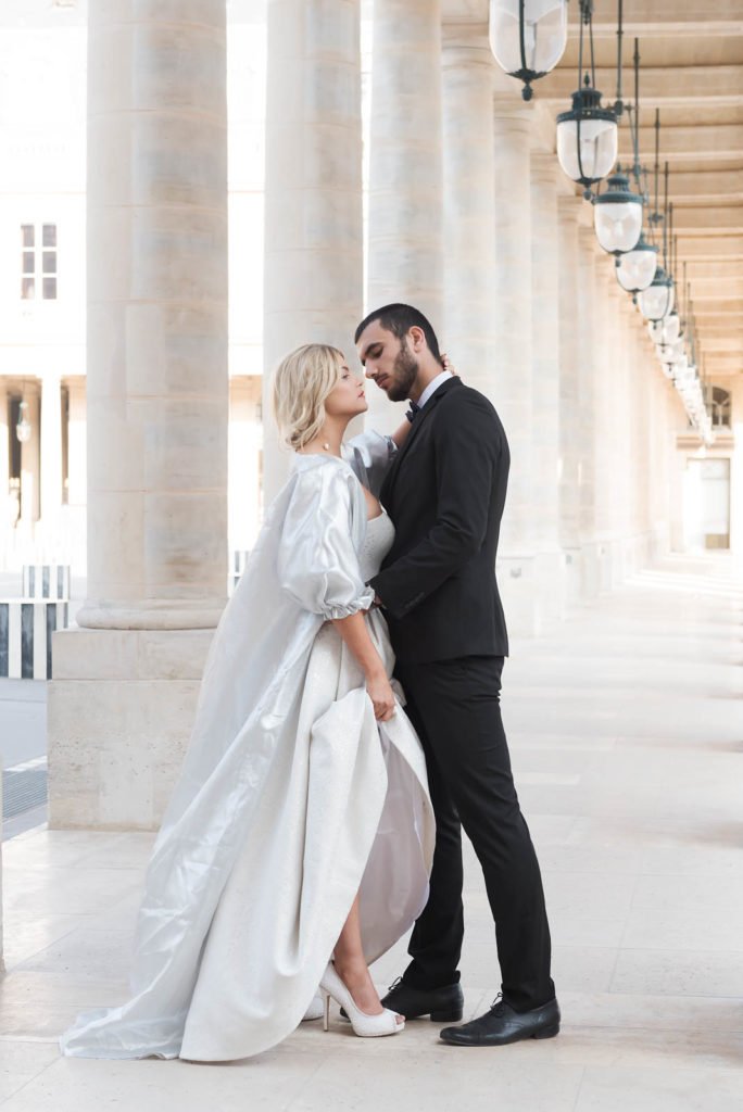 A high fashion intimate wedding couple embraces under the columns of a French building in Paris.
