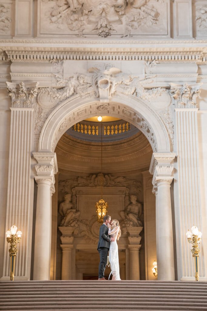 Newlyweds kiss at the top of grand staircase at San Francisco City Hall wedding.