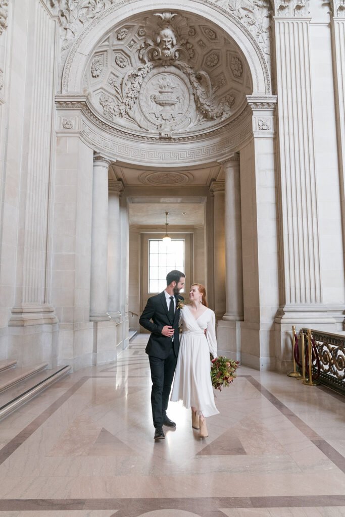 Newlyweds walk through a marble arch in SF City Hall.